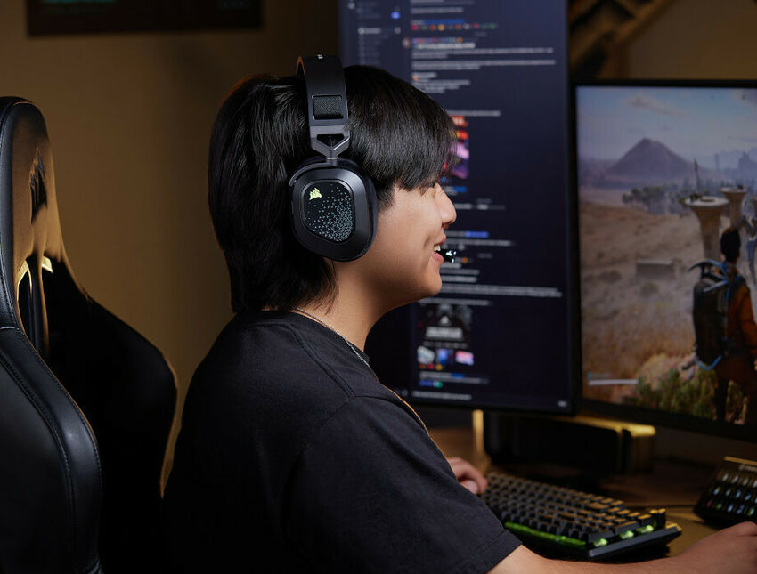 Un jeune homme portant un casque Corsair joue sur un PC avec deux écrans et un clavier rétroéclairé.