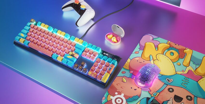 Un clavier mécanique rétroéclairé avec des touches roses et bleues, accompagné d'une souris gaming violette sur un tapis de souris coloré, une manette blanche et des écouteurs sans fil.