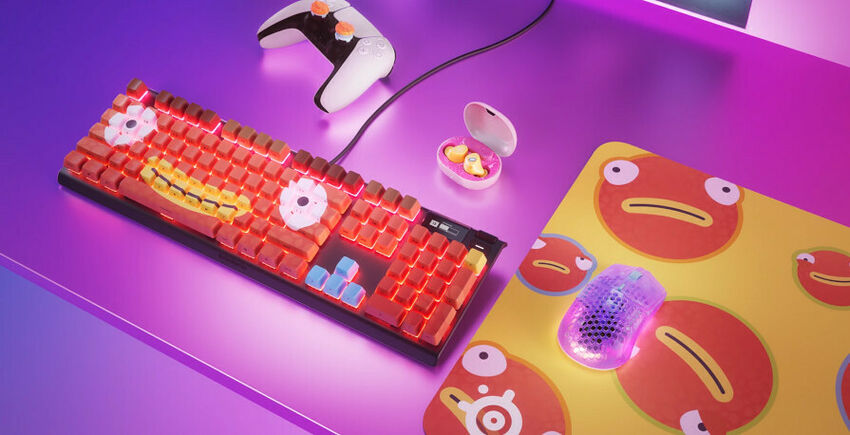Un clavier mécanique rétroéclairé rouge et blanc, une souris gaming violette, une manette blanche et un tapis de souris illustré de personnages rouges sur un bureau violet.