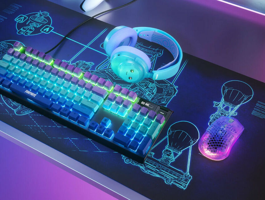 Un clavier mécanique rétroéclairé avec des touches bleues et vertes, un casque audio bleu clair et une souris gamer lumineuse, le tout posé sur un tapis de souris graphique.