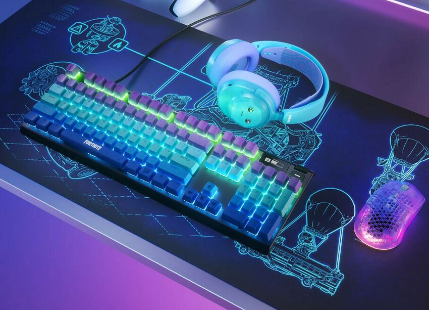 Un clavier mécanique rétroéclairé aux couleurs de Fortnite, un casque bleu ciel et une souris gaming violette posés sur un tapis de souris noir avec des motifs bleus.