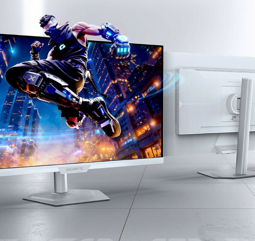 Écran de PC Gigabyte affichant un personnage de jeu vidéo en pleine action dans une ville futuriste, avec le dos de l'écran blanc visible à côté.
