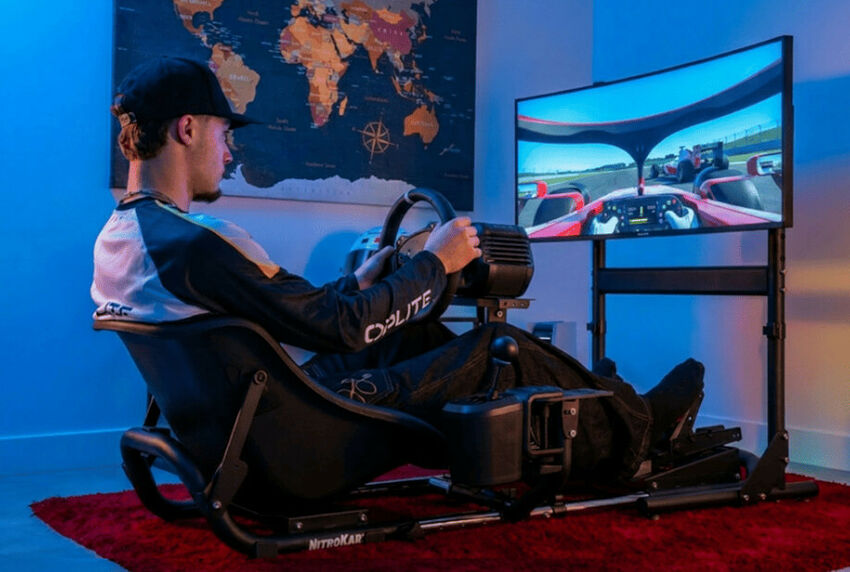 Un homme assis dans un cockpit de simulation de course avec un volant, un siège de type baquet et un grand écran affichant un jeu de course automobile.