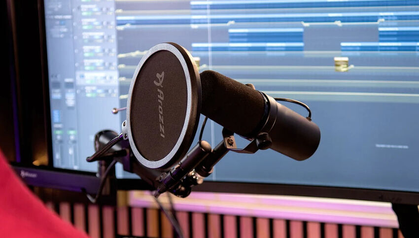 Microphone de studio noir avec filtre anti-pop Arozzzi monté sur un bras articulé devant un écran affichant un logiciel de montage audio.