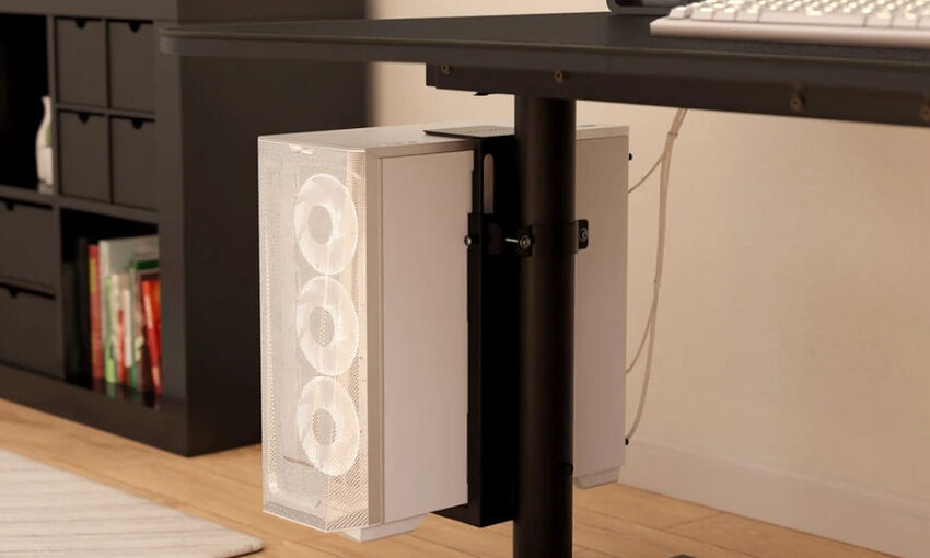 Un boîtier PC blanc fixé sous un bureau noir par un support spécialisé. Le boîtier présente une façade en mesh avec trois ventilateurs blancs visibles.