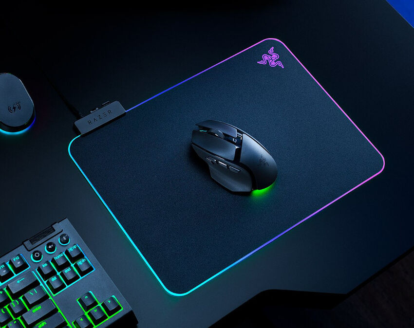 Un tapis de souris Razer avec un éclairage RGB sur les bords, accompagné d'une souris Razer noire posée dessus. Un clavier rétroéclairé est partiellement visible sur le côté.