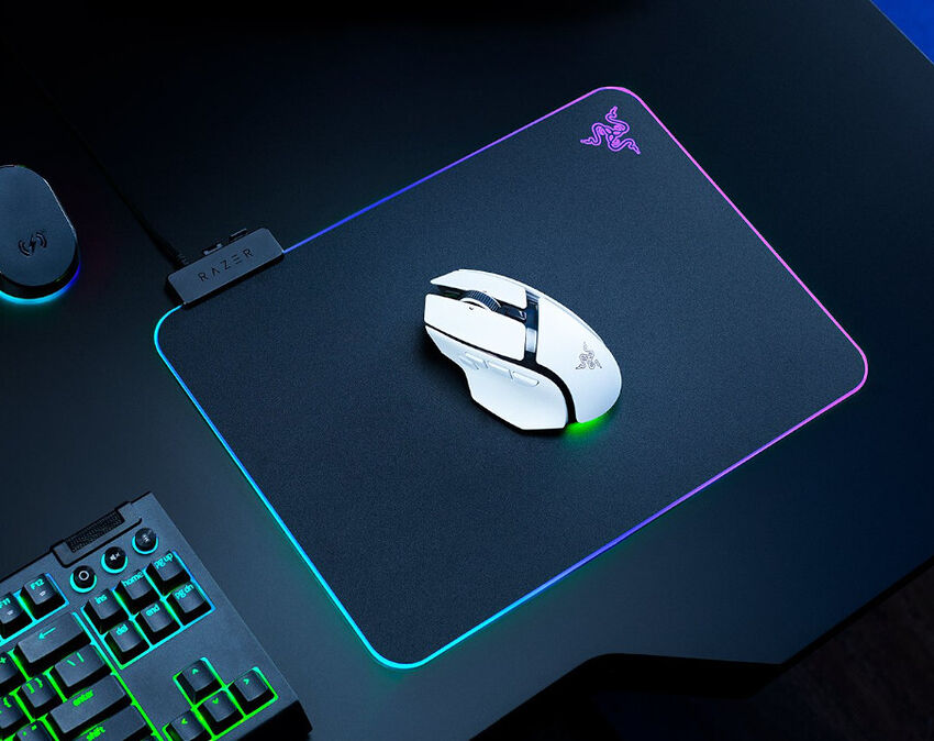 Un tapis de souris Razer avec éclairage RGB sur les bords, accompagné d'une souris Razer blanche posée dessus. On aperçoit également une partie d'un clavier rétroéclairé en bas à gauche.