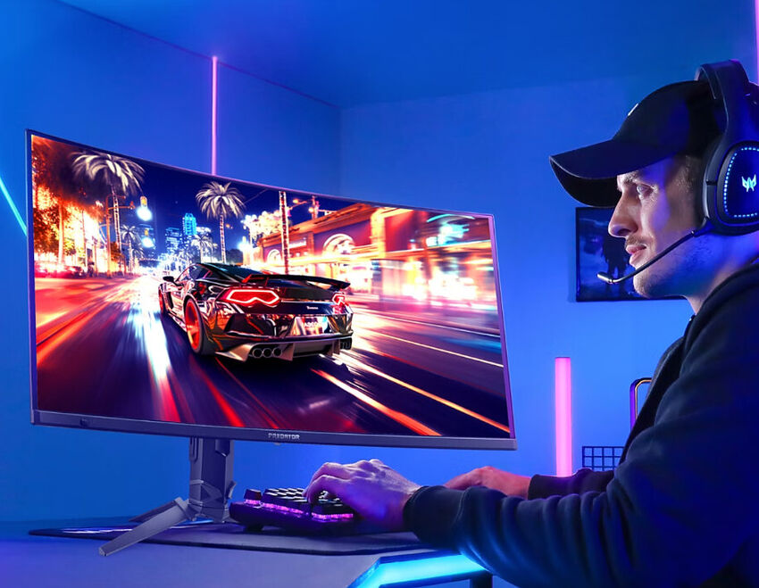 Un homme portant un casque audio joue sur un PC avec un écran incurvé affichant une scène de voiture de sport en pleine ville, le tout dans une ambiance lumineuse bleue et rose.