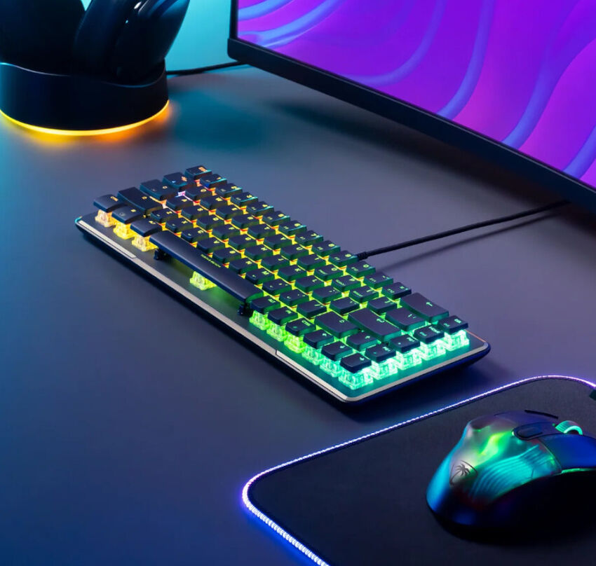 Un clavier mécanique rétroéclairé avec des touches RGB, posé sur un bureau à côté d'une souris gaming et d'un écran.